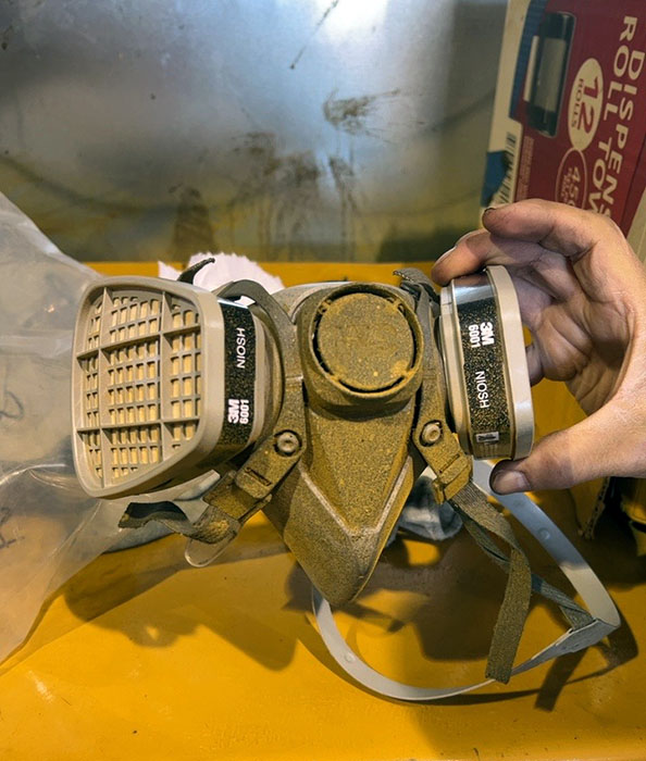 Photo shows dirty respirator and filters covered in paint overspray. The employee pulled the respirator out of his storage bag like this.